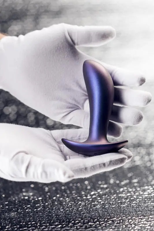 Bouchon anal violet tenu par des mains gantées.